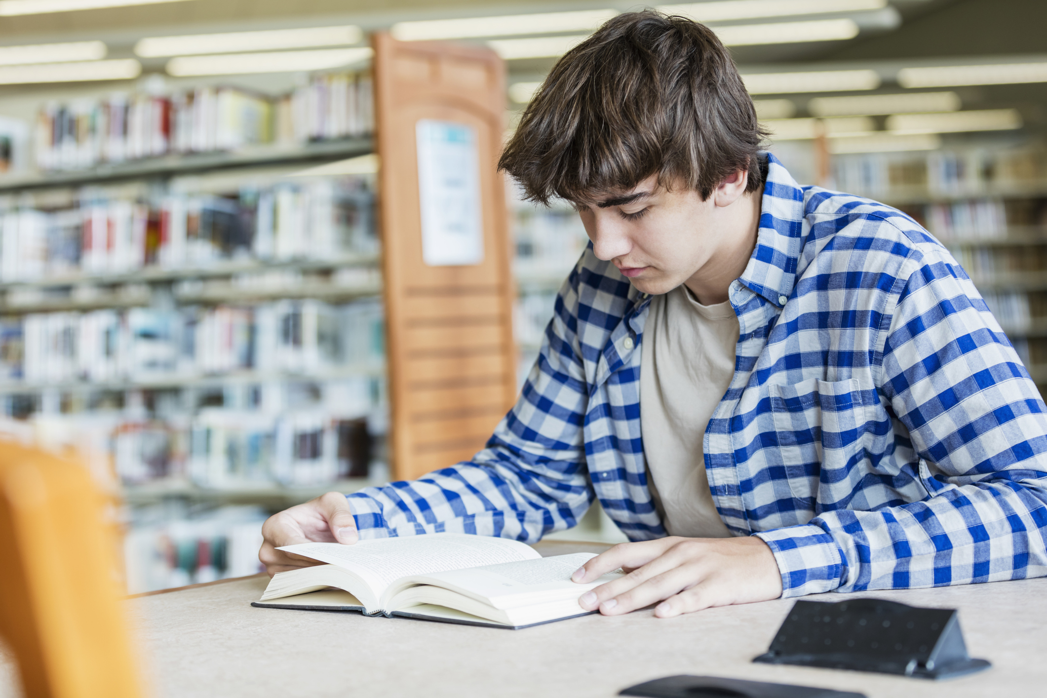 Tenåringsgutt leser bok i bibliotek