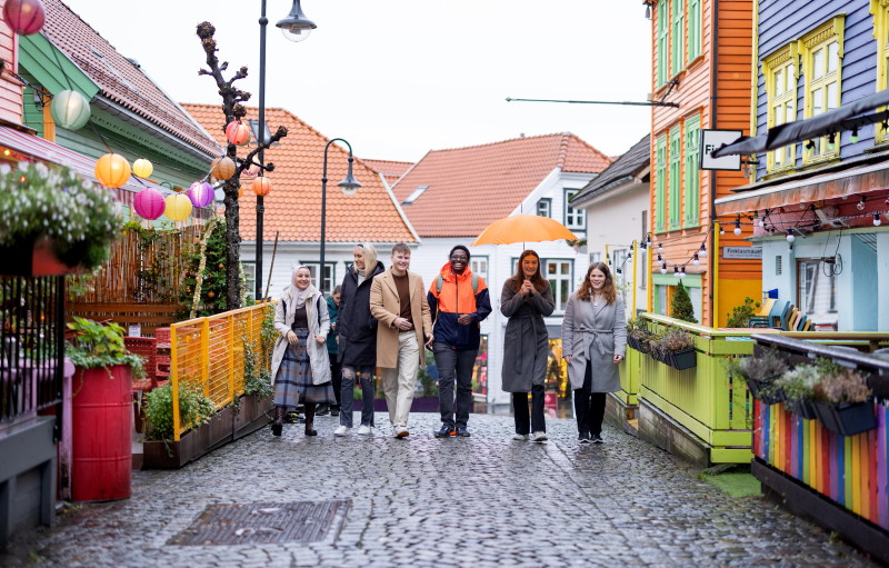 Seks studenter går mot kamera ved siden av hverandre i en gate med fargerike hus i Stavanger sentrum.