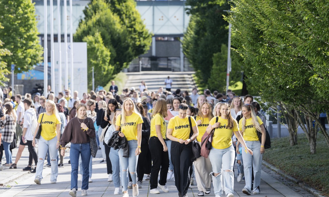 En stor gruppe studenter, flere med gule Fadder-t-skjorter, går på campus