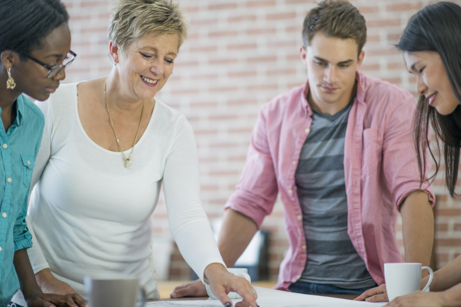 En gruppe voksne står rundt et bord og diskuterer. Foto: iStock