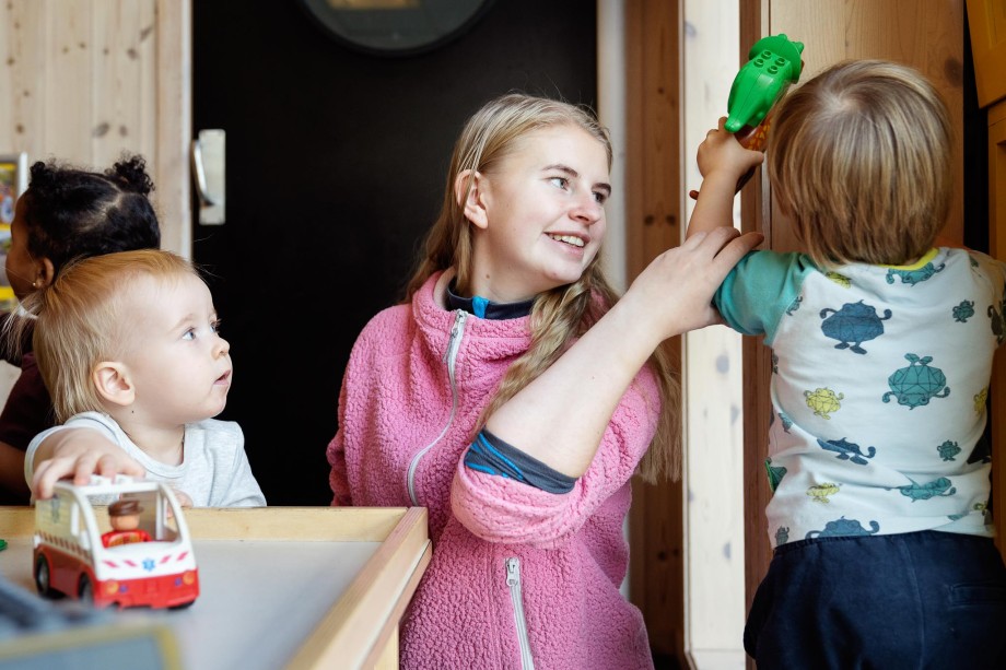 Ung kvinnelig barnehagelærerstudent er i praksis i barnehage og leker med to småbarn