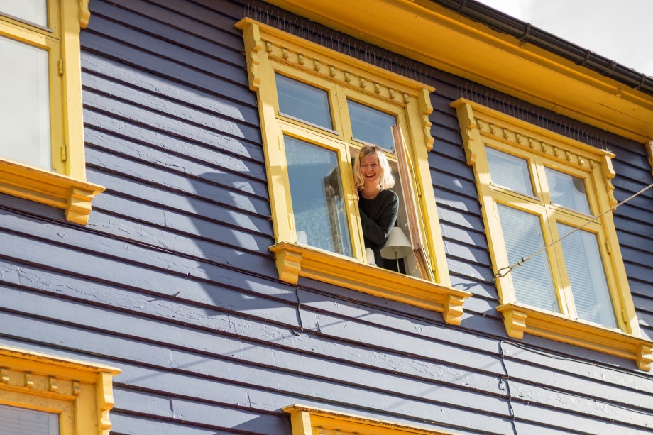 Ung kvinne titter ut av et vindu i et fargerikt trehus