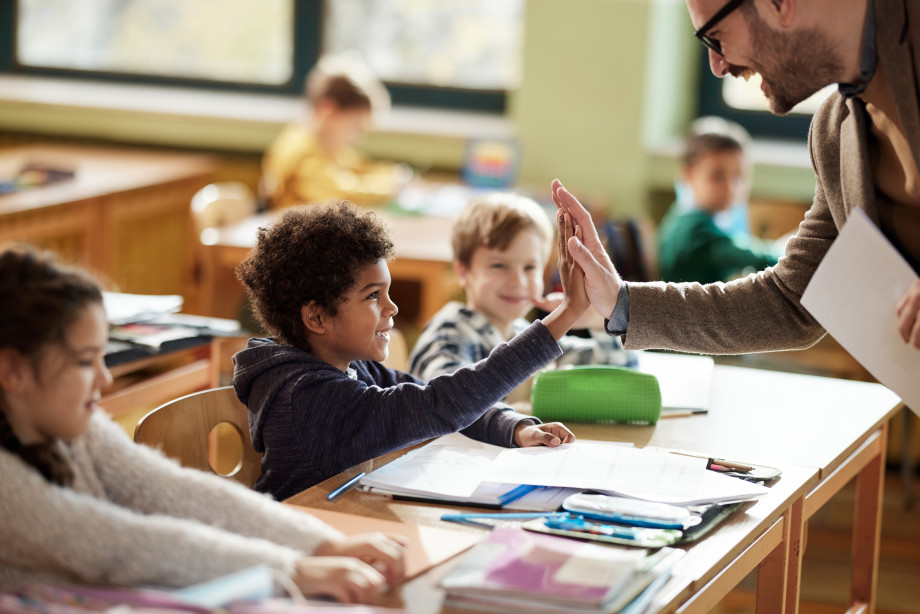 En mannlig lærer slår high five med en liten gutt som sitter ved en pult