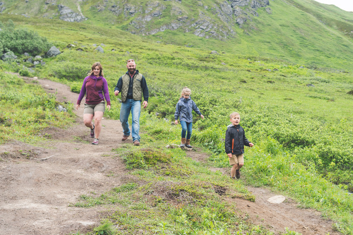 to voksne og to barn går på en sti i høyfjellsnatur